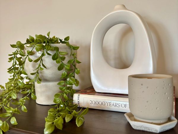 Minimalist decor with a plant, abstract sculpture, and a candle on a wooden surface.