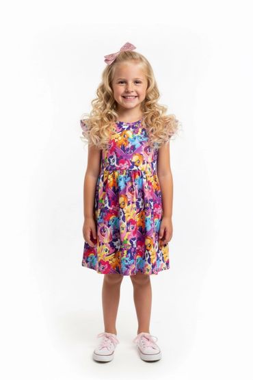 Smiling little girl in a colorful cartoon character dress and pink sneakers.