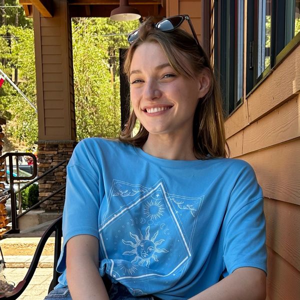 Smiling woman in a blue sun-themed t-shirt sitting outdoors.