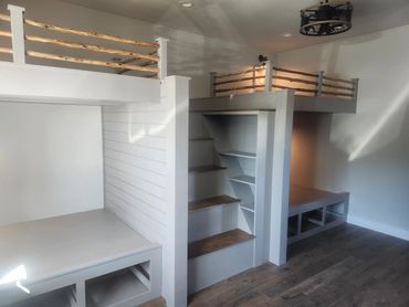 Custom-built white bunk beds with rustic wooden railings and built-in stairs.