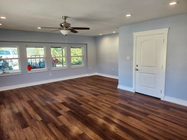 Empty room with wooden flooring, light blue walls, ceiling fan, and windows.