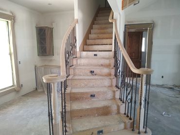 Unfinished staircase with wooden railing and iron balusters in a house under construction.