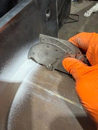Person using a tool on a metal surface wearing orange gloves.
