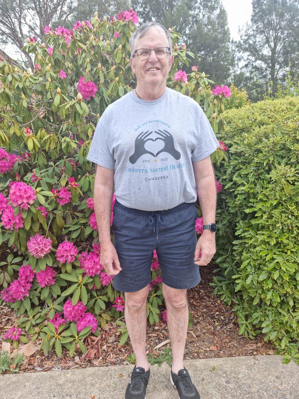 Man standing in front of vibrant pink flowers and green shrubs.