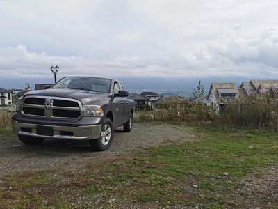 A gray Dodge Ram pickup truck parked on a gravel patch near residential houses under a cloudy sky.