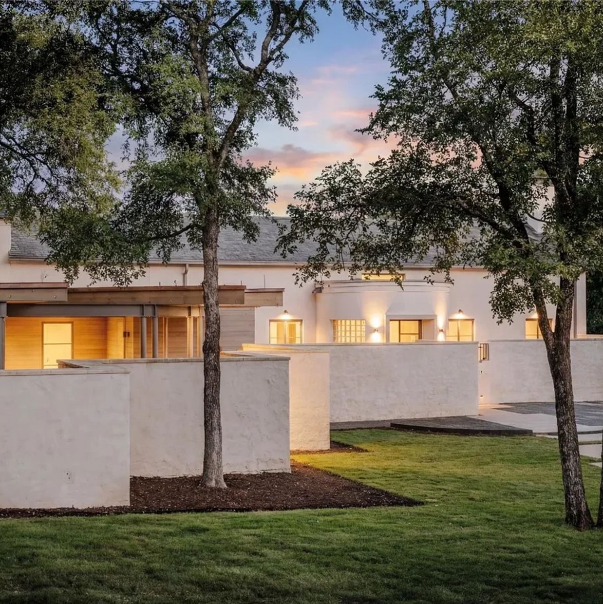 Modern white house with courtyard walls and trees at sunset.