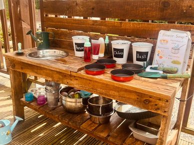 Photo of mud kitchen with herbs growing and painted rocks
