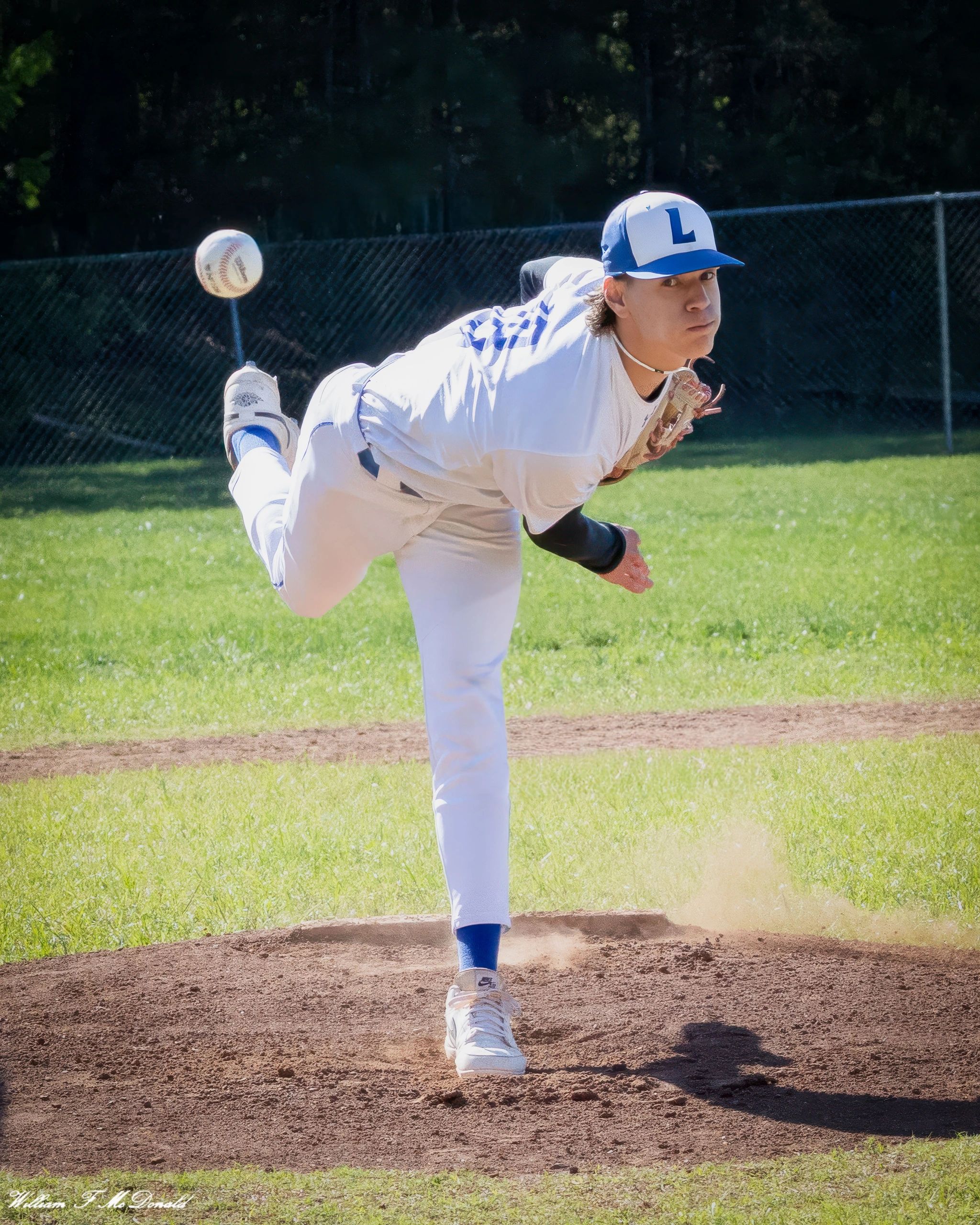 Baseball pitcher mid-throw on a sunny field.