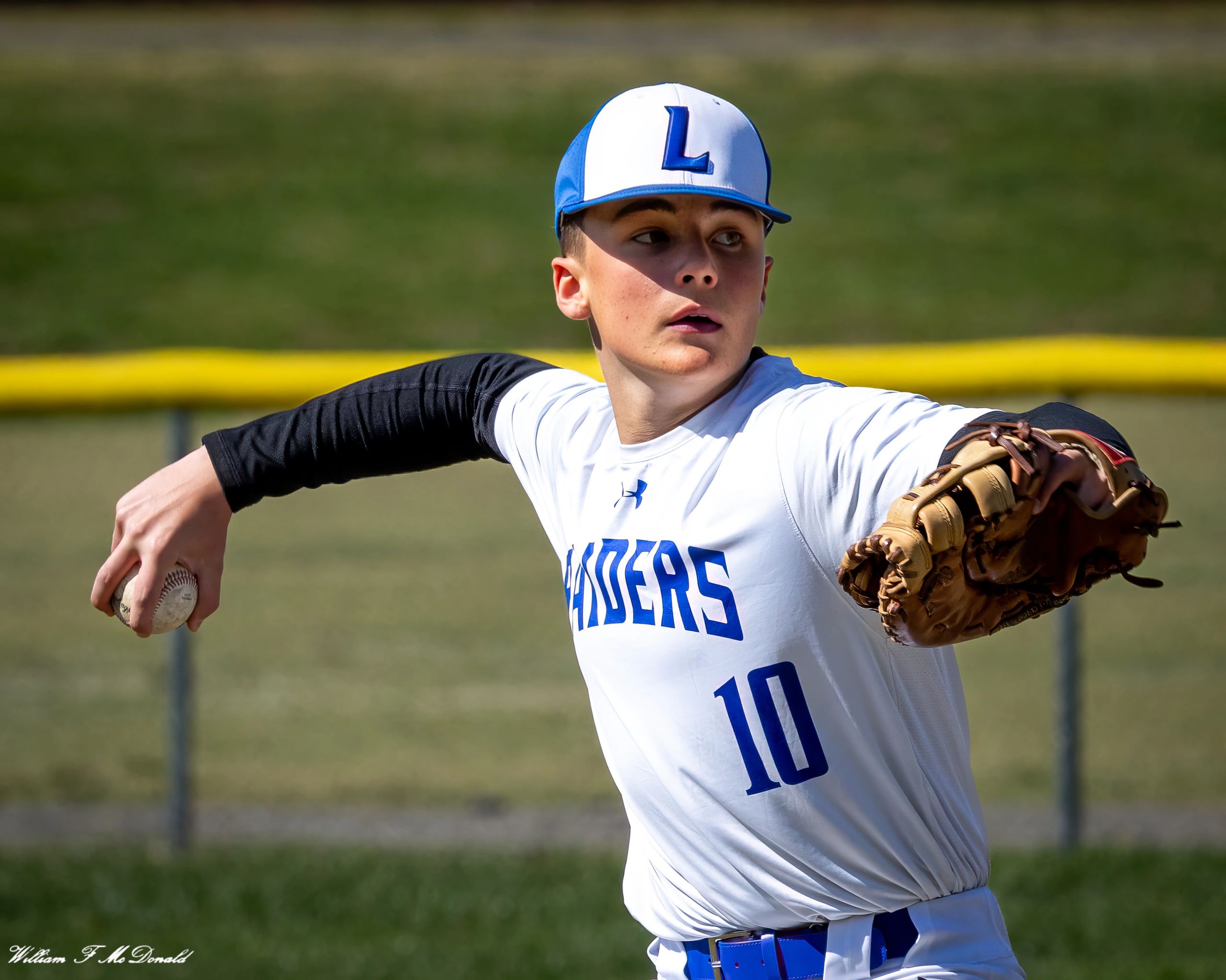 Baseball pitcher in mid-throw wearing a blue and white hat and Raiders jersey.