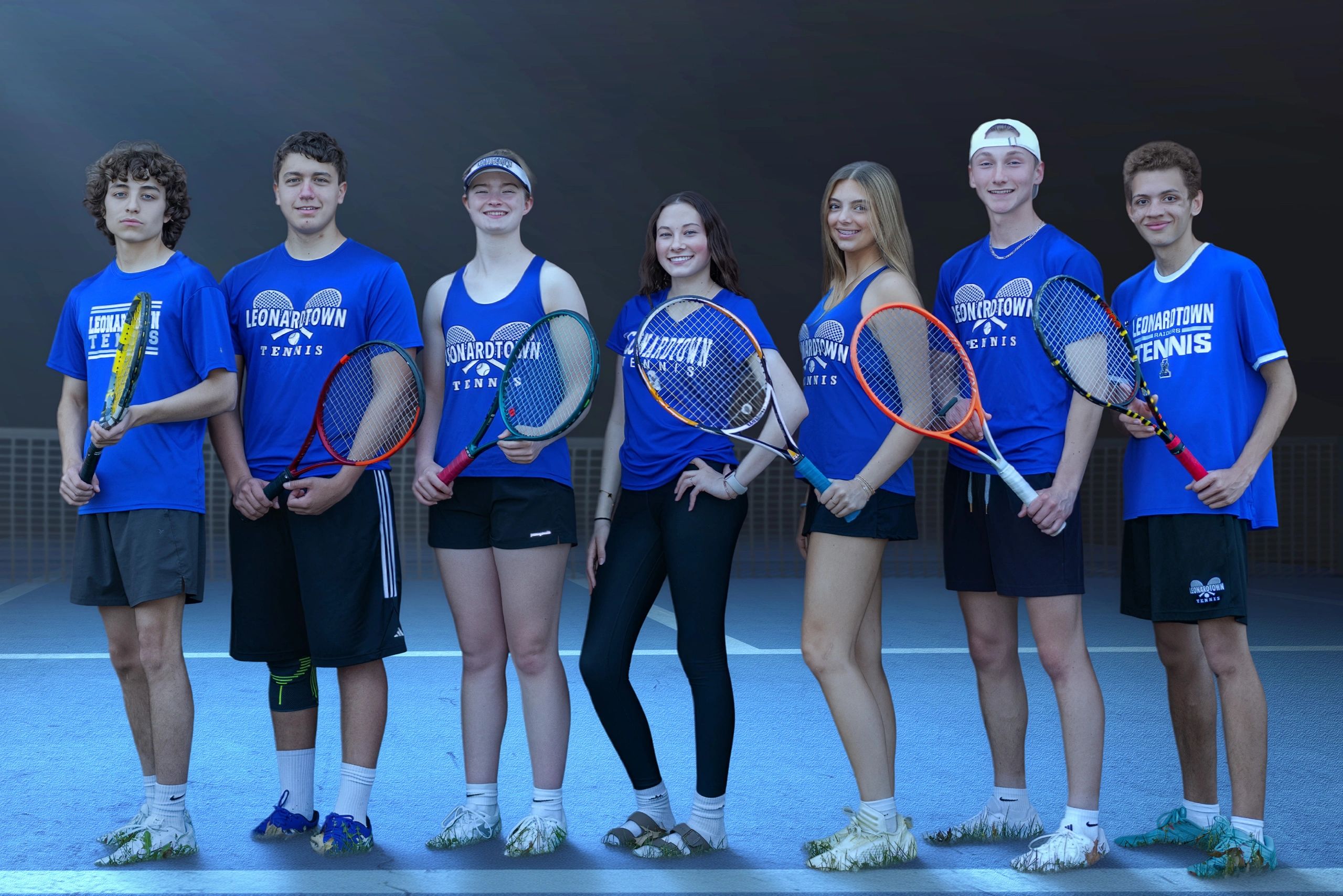 Seven young tennis players in Leonardtown Tennis shirts hold rackets, standing on a blue court.