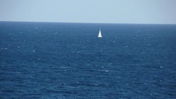A solitary sailboat on a vast, calm ocean under a clear sky.