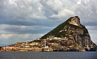 The Rock of Gibraltar under a cloudy sky by the sea.