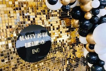 Gold sequin wall backdrop with black, white and gold balloon garland and black sign