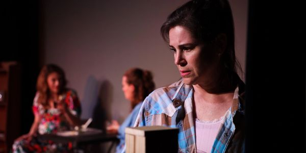 A woman in focus looks thoughtfully away as two women talk in the background.