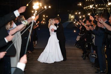 Newlyweds share a kiss surrounded by guests holding sparklers at night.