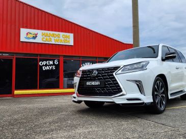 White Lexus SUV parked outside a red Hands On Car Wash building.
