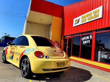 Yellow Volkswagen Beetle parked outside a red and yellow hands-on car wash.