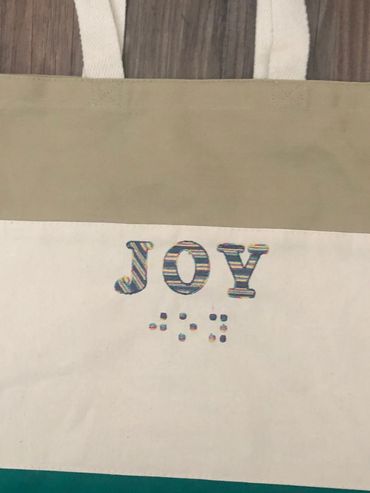 Tricolor green bag with JOY in print and joy in Braille.