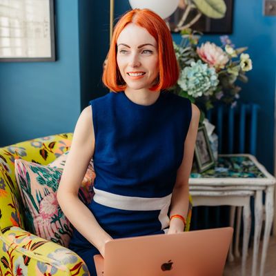 A woman smiling sitting with her laptop on her lap.
