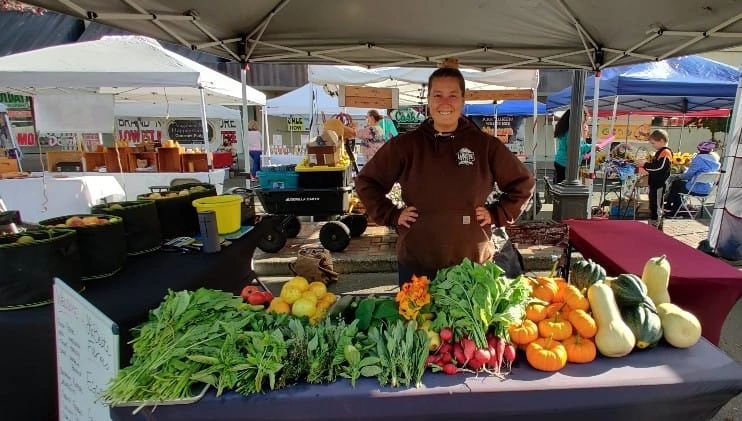 Vendor at farmers market with fresh produce.
