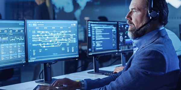 Man in headset monitoring data on multiple computer screens.