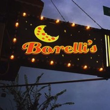 Illuminated Borelli's sign glowing against a dusky sky at a street corner.
