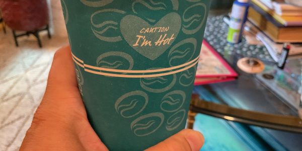 Hand holding a green coffee cup with text.