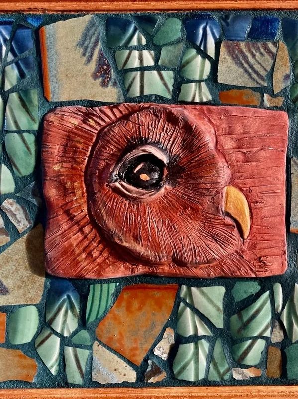 A textured ceramic owl head on a mosaic tile background.