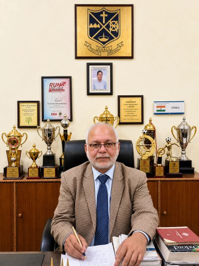 Professional man in suit sitting at desk surrounded by trophies and awards.