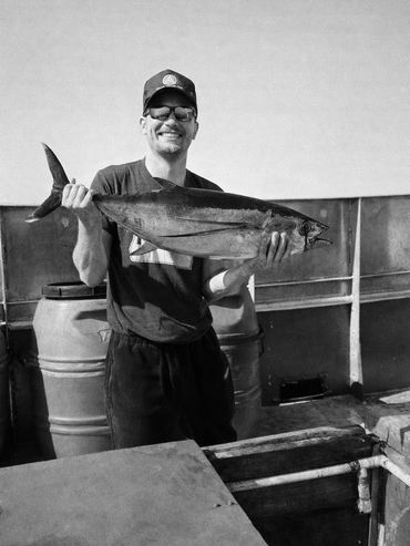 Man proudly holding a large fish on a boat, smiling at the camera.