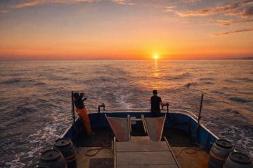 Two fishermen on a boat at sunset on the ocean.