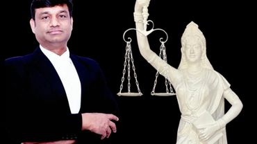 Man in lawyer's attire stands next to a statue of Lady Justice holding scales.