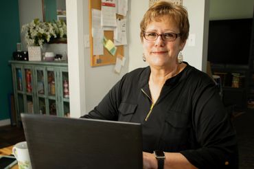 Smiling woman working on a laptop at home with glasses and earrings.