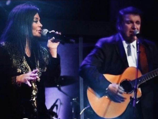 Two musicians performing on stage, one singing and the other playing guitar.