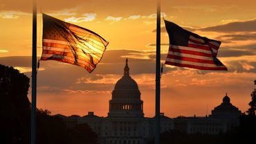 Two American flags at half-staff with the Capitol building at sunset.