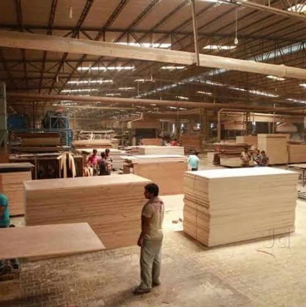 Workers in a large warehouse handling stacks of plywood sheets.