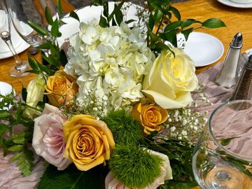 Elegant floral centerpiece with roses and greenery on a wooden table setting.