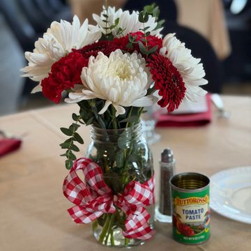 A bouquet of red and white flowers in a jar with a red checkered ribbon.