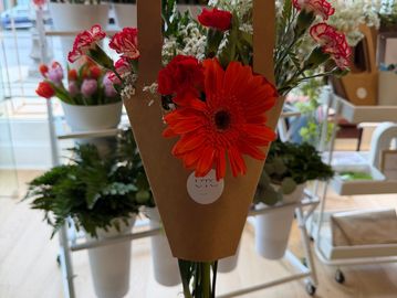Hand holding a bouquet of vibrant red and orange flowers in a flower shop.