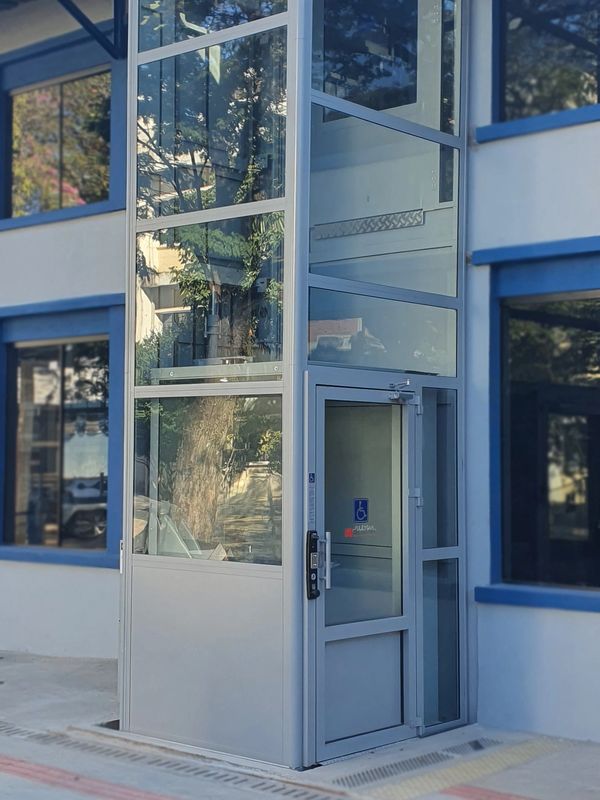A modern glass elevator with accessibility features outside a building.