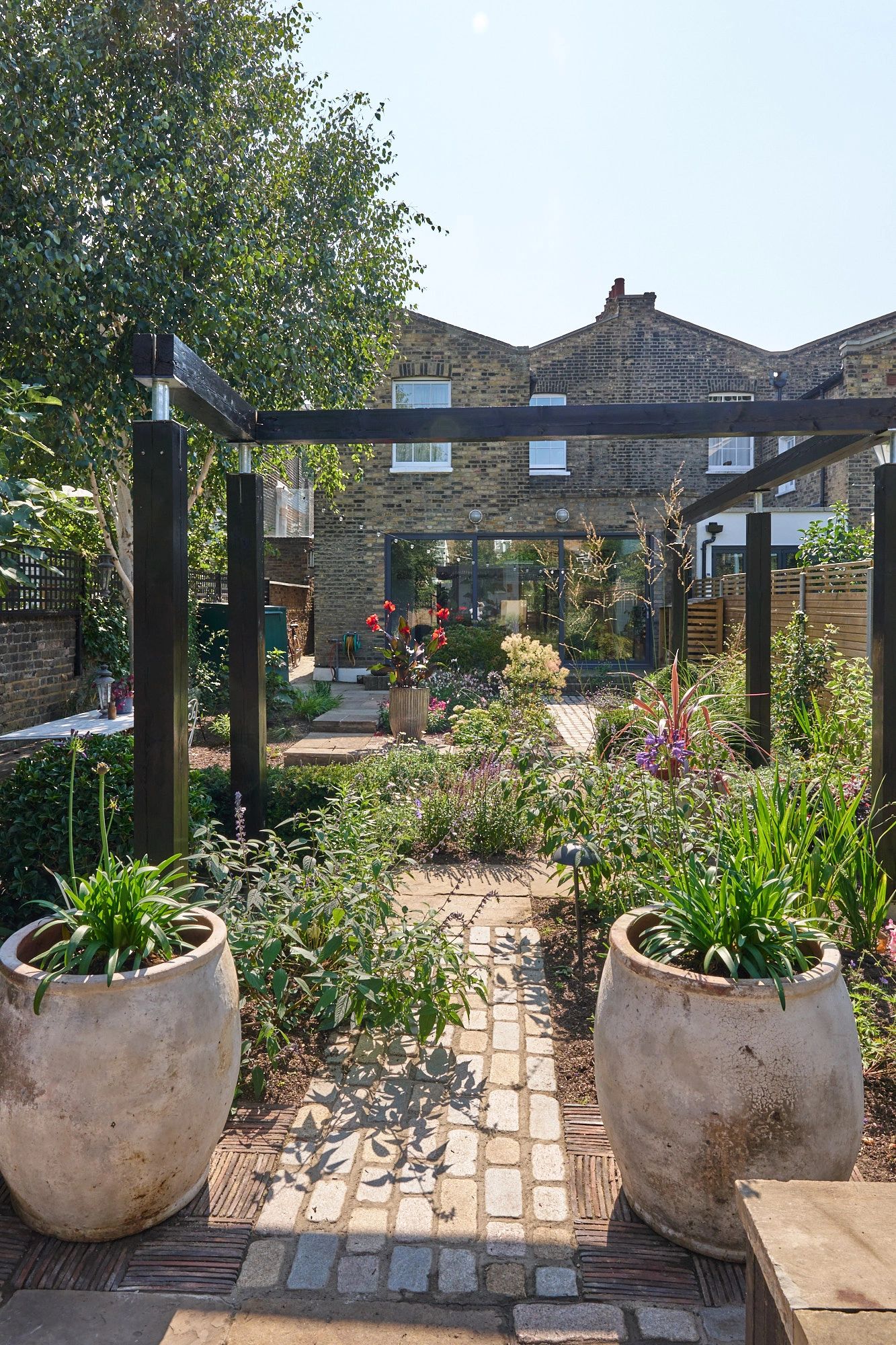 City garden with large pots, cobble pathway, pond and black pergola
