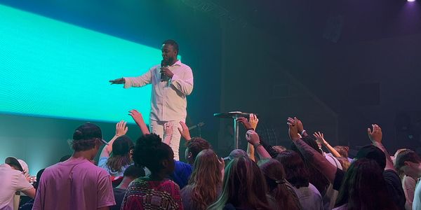 A speaker addressing an engaged audience with raised hands in a dimly lit venue.