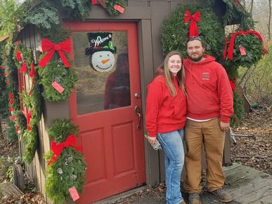 Couple in matching red sweaters posing by a decorated doorway.