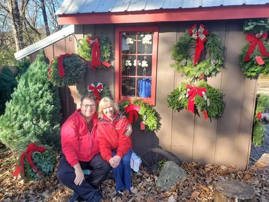 A couple sitting in front of a shed decorated with Christmas wreaths and ribbons.