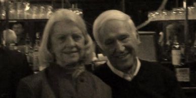 Older couple smiling together in a dimly lit setting.