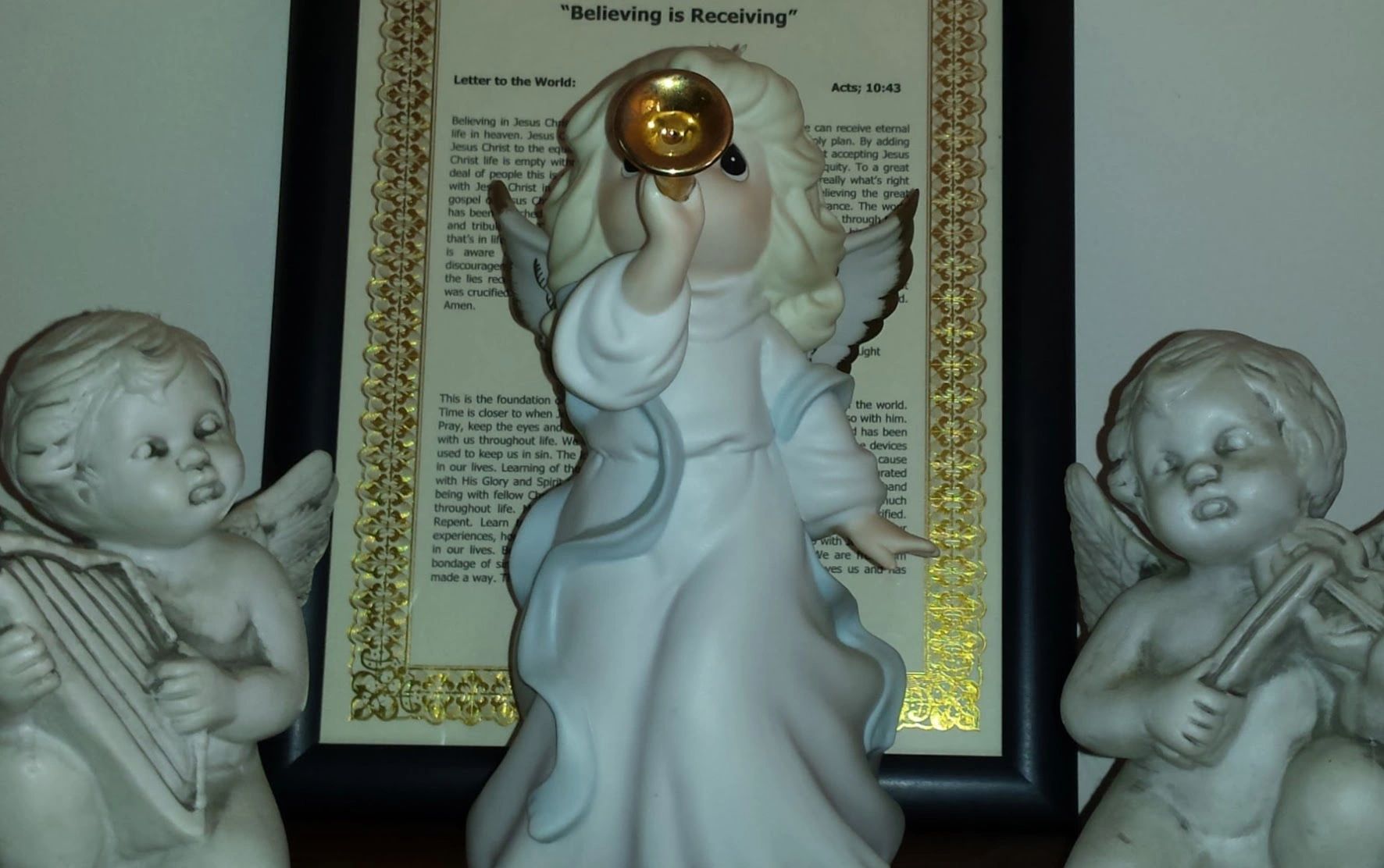 Three angel figurines playing instruments in front of a framed document.