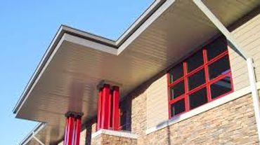 Modern building exterior with red window frames and pillars under a slanted roof.