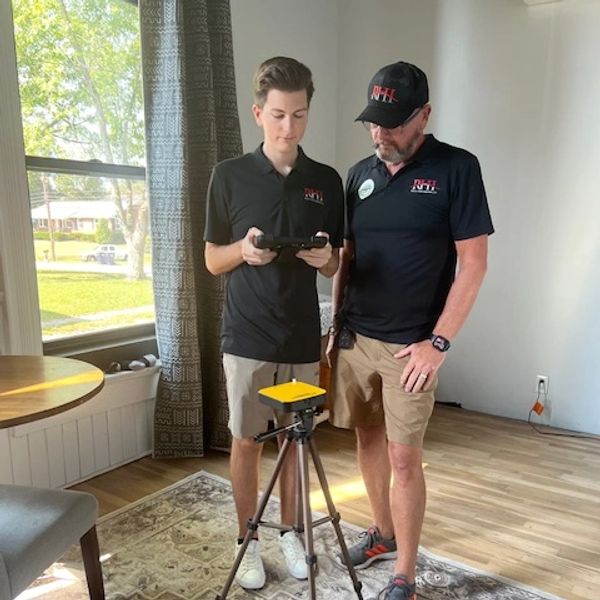 Two men setting up a Radon monitor on a tripod indoors.
