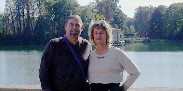 A couple posing by a river with trees in the background.