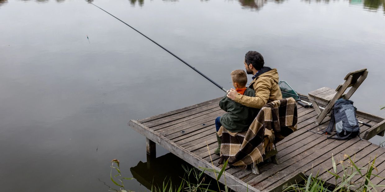 Man and child fishing on a wooden dock by the lake.